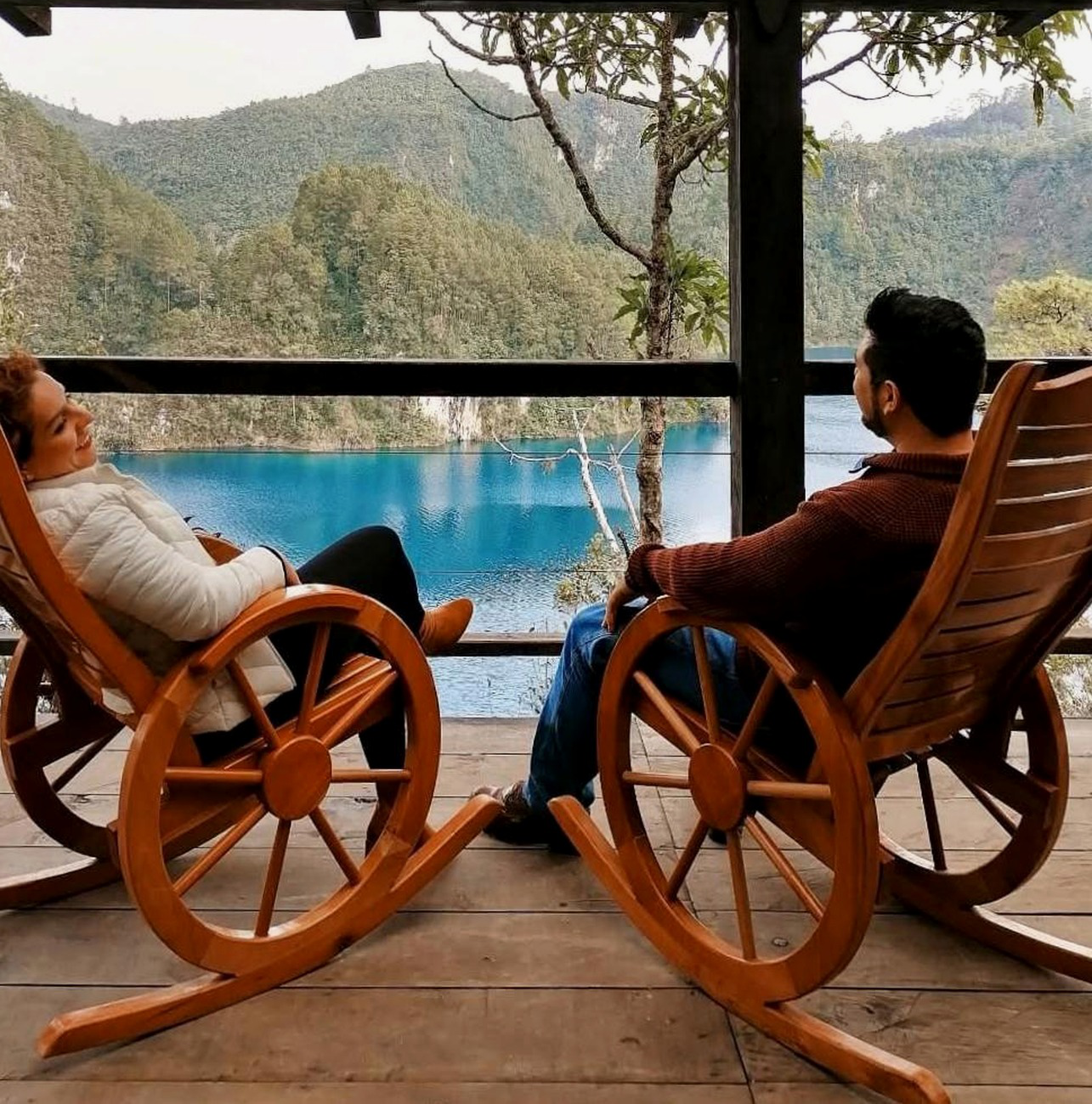 Vista al lago desde la terraza, con dos sillas de madera frente al agua turquesa.
